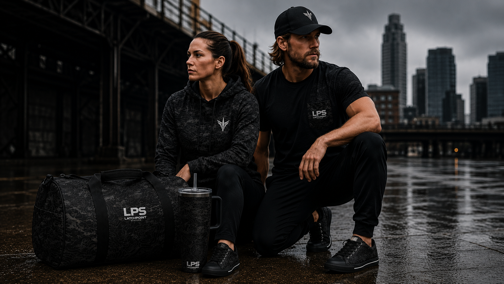 Two people sitting on a dock with a TERRA BLACK duffel bag and tumbler, city skyline in the background.